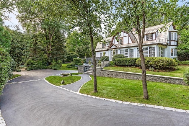 view of front facade featuring driveway, a chimney, a front lawn, and a gambrel roof