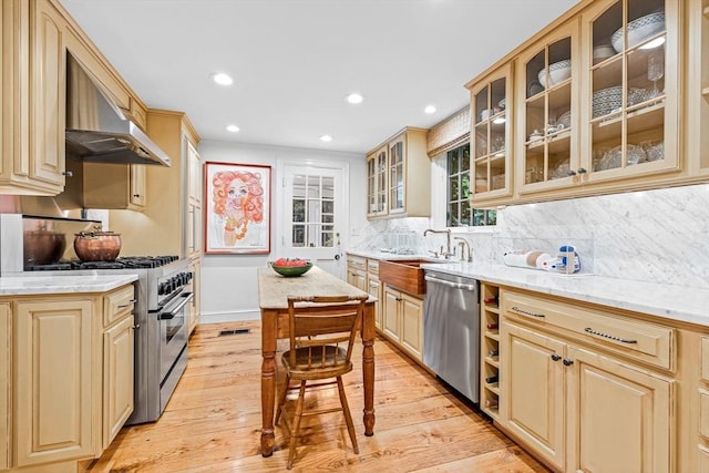 kitchen featuring light wood-style flooring, stainless steel appliances, ventilation hood, decorative backsplash, and glass insert cabinets