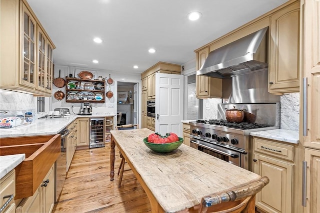 kitchen featuring wine cooler, stainless steel appliances, backsplash, light wood-style floors, and wall chimney exhaust hood