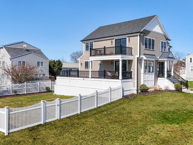 rear view of house with a shingled roof, board and batten siding, a fenced backyard, a balcony, and a lawn