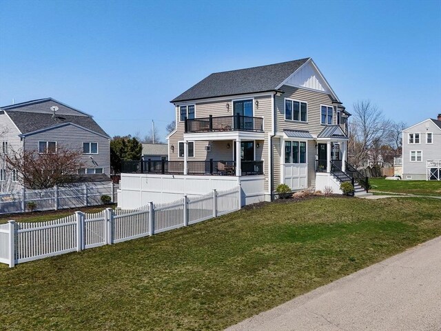 colonial home featuring fence, a shingled roof, a front yard, and a balcony