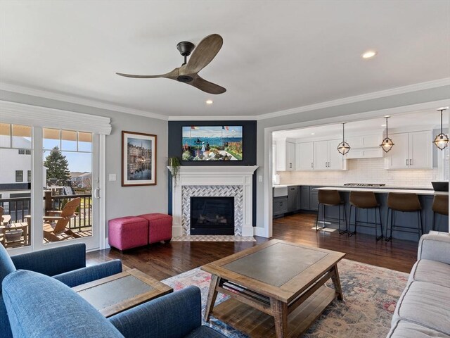 living area with ceiling fan, dark wood finished floors, recessed lighting, a tile fireplace, and ornamental molding
