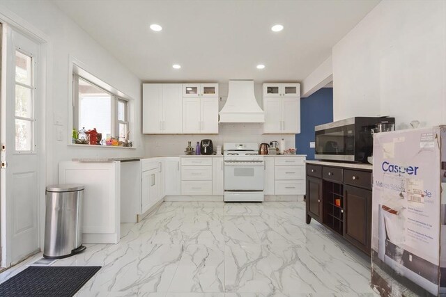 kitchen with stainless steel microwave, recessed lighting, glass insert cabinets, custom range hood, and white gas range oven