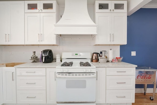 kitchen with light countertops, premium range hood, gas range gas stove, white cabinets, and glass insert cabinets