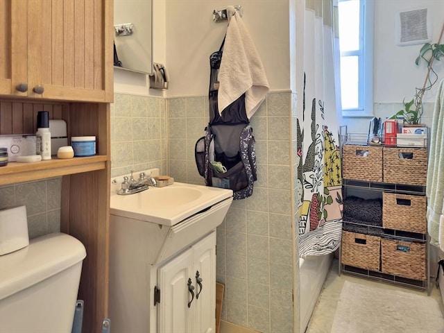 full bath with toilet, a wainscoted wall, vanity, tile walls, and tile patterned floors