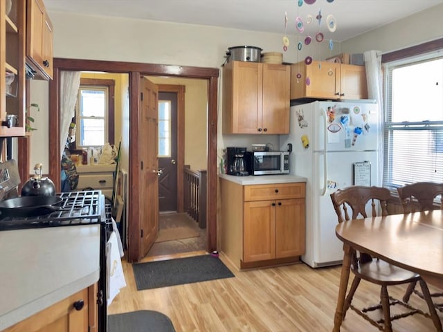 kitchen with light countertops, stainless steel microwave, light wood-style floors, freestanding refrigerator, and gas stove