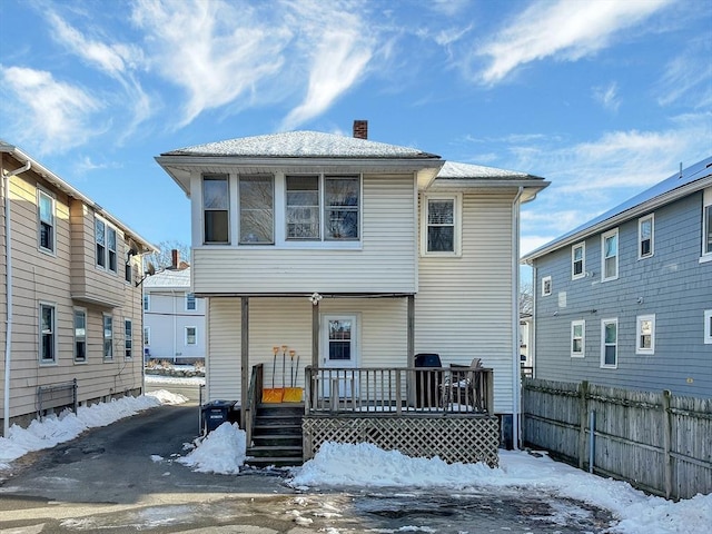 snow covered back of property featuring a deck, a chimney, and fence