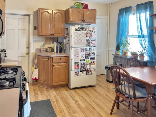 kitchen with brown cabinets, light countertops, light wood-style flooring, and black appliances