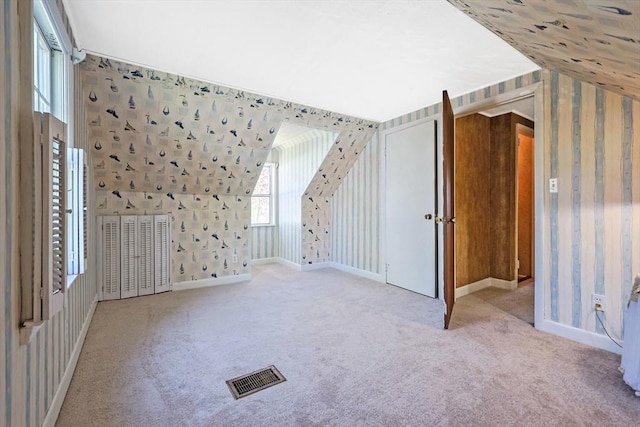 additional living space featuring light colored carpet, baseboards, visible vents, and wallpapered walls