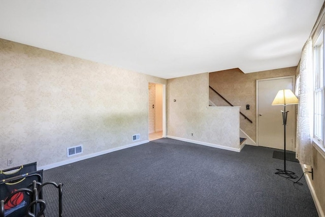 spare room with wallpapered walls, dark colored carpet, stairs, and visible vents