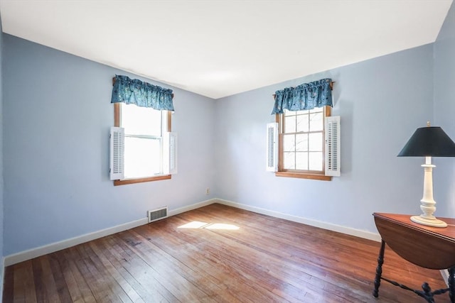 unfurnished room with visible vents, wood-type flooring, and baseboards