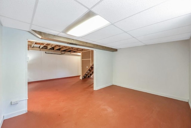 finished below grade area featuring baseboards, a paneled ceiling, and stairway