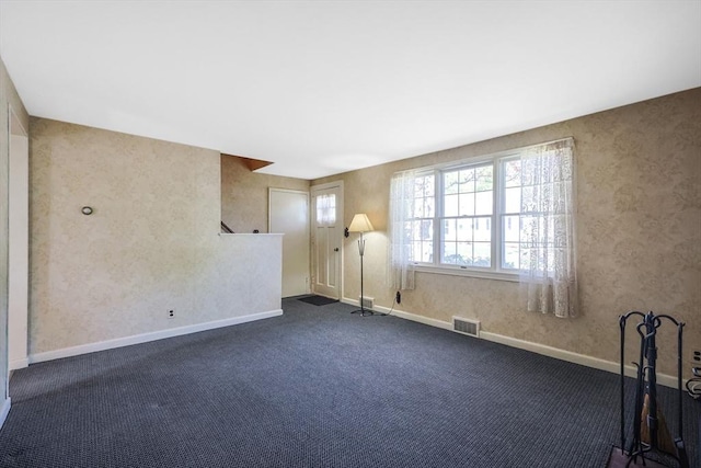 interior space with baseboards, wallpapered walls, dark carpet, and visible vents