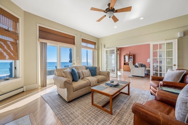 living room with french doors, a water view, light wood-type flooring, and ceiling fan