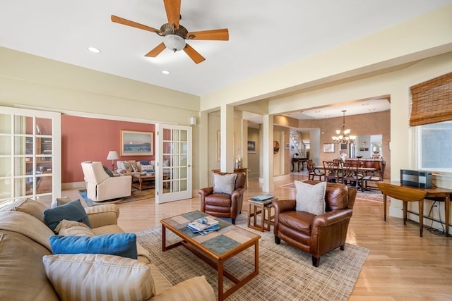 living room with ceiling fan with notable chandelier and light hardwood / wood-style floors