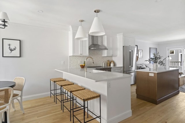 kitchen with high end refrigerator, pendant lighting, kitchen peninsula, white cabinetry, and wall chimney exhaust hood