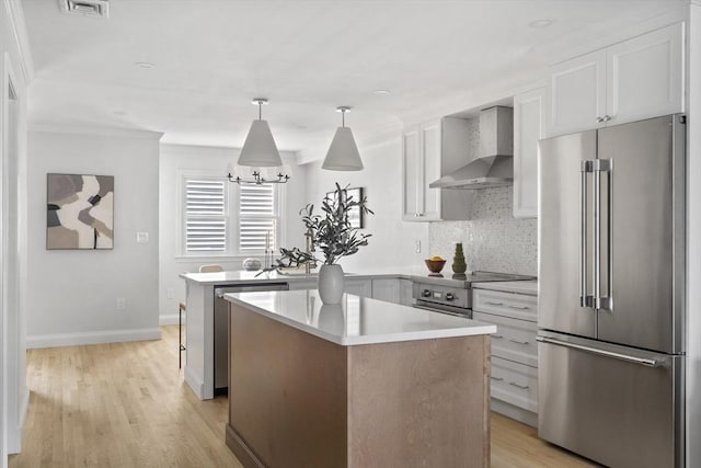 kitchen with white cabinetry, premium appliances, wall chimney range hood, and a kitchen island