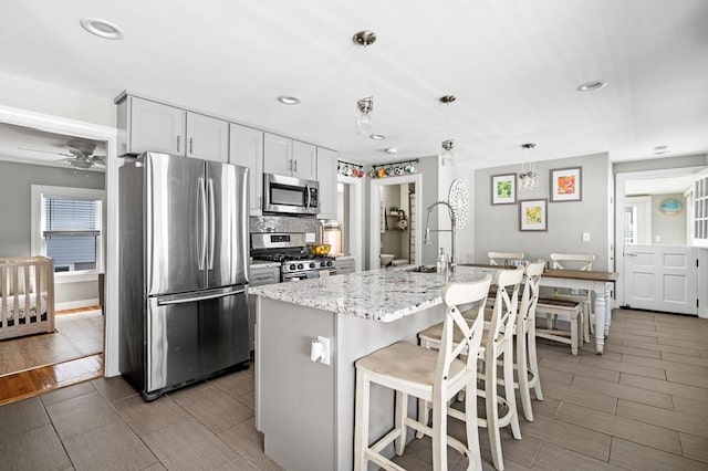 kitchen featuring ceiling fan, appliances with stainless steel finishes, hanging light fixtures, light stone countertops, and a sink