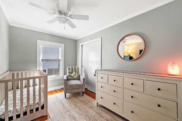 bedroom featuring ceiling fan, crown molding, a nursery area, baseboards, and light wood finished floors