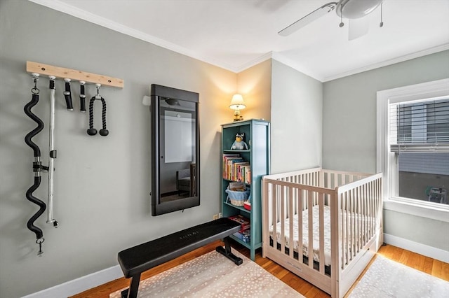 bedroom featuring crown molding, a crib, baseboards, and wood finished floors