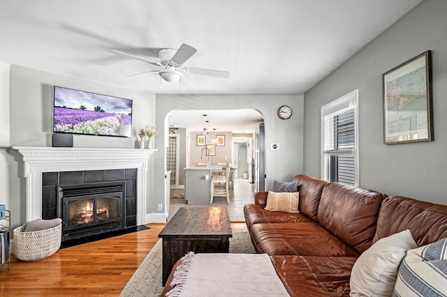 living area featuring a tiled fireplace, arched walkways, a ceiling fan, and wood finished floors