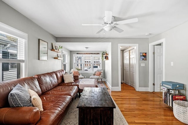 living room featuring light wood-style floors, baseboards, ceiling fan, and a healthy amount of sunlight