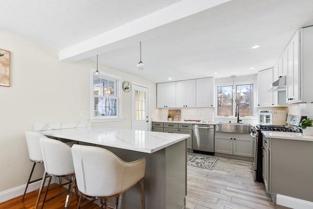 kitchen featuring a peninsula, stainless steel appliances, a sink, a kitchen bar, and decorative light fixtures