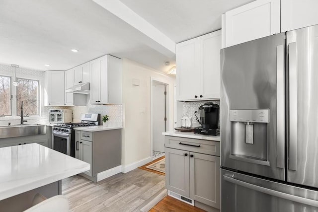 kitchen featuring light countertops, appliances with stainless steel finishes, a sink, and under cabinet range hood