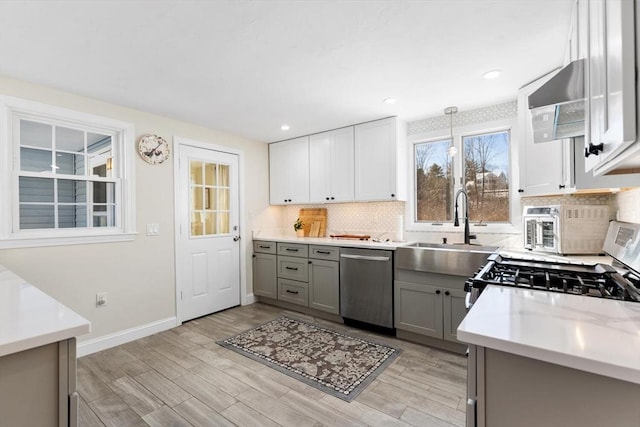 kitchen featuring tasteful backsplash, appliances with stainless steel finishes, gray cabinets, and decorative light fixtures