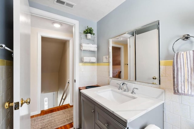 bathroom featuring wainscoting, vanity, visible vents, and tile walls