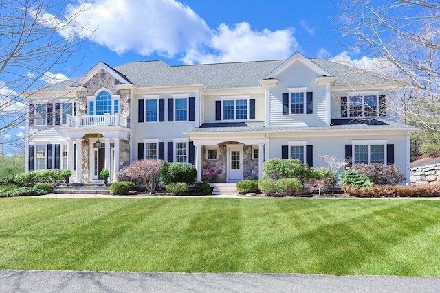 view of front facade featuring stone siding, a balcony, and a front yard