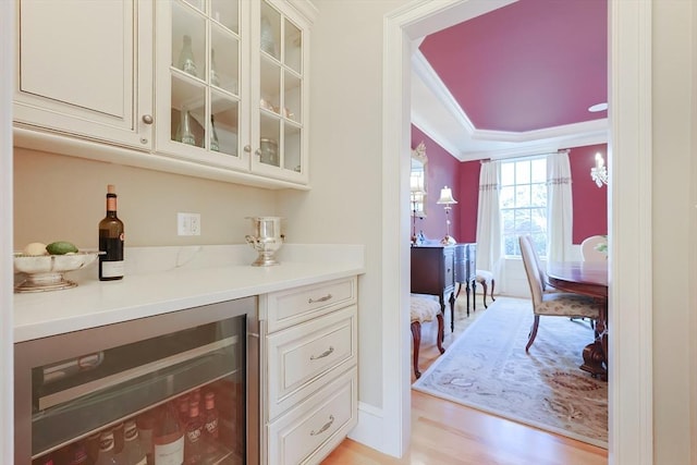 bar featuring beverage cooler, crown molding, light wood-style flooring, and a dry bar