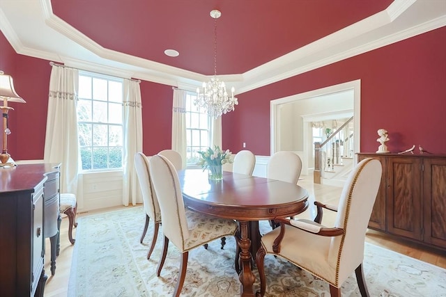dining area featuring an inviting chandelier, ornamental molding, a tray ceiling, and stairs
