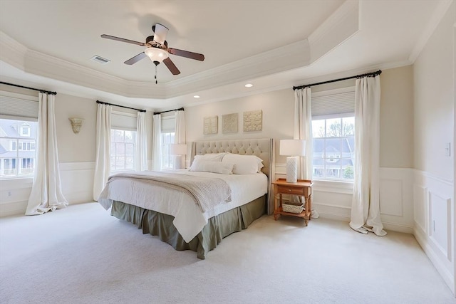 carpeted bedroom with a wainscoted wall, visible vents, a decorative wall, and a raised ceiling