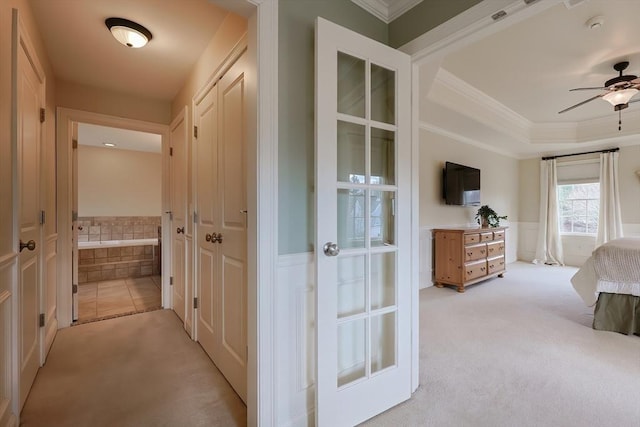 hallway with a wainscoted wall, light carpet, crown molding, and a raised ceiling