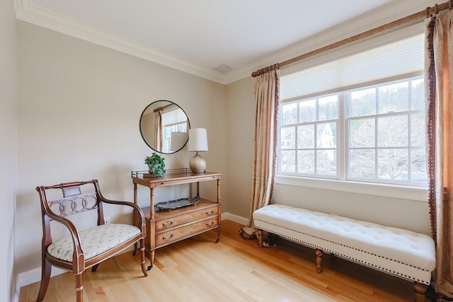 sitting room with baseboards, visible vents, crown molding, and light wood-style floors