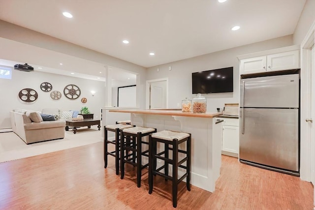 kitchen with freestanding refrigerator, a kitchen bar, light wood-style flooring, white cabinets, and recessed lighting