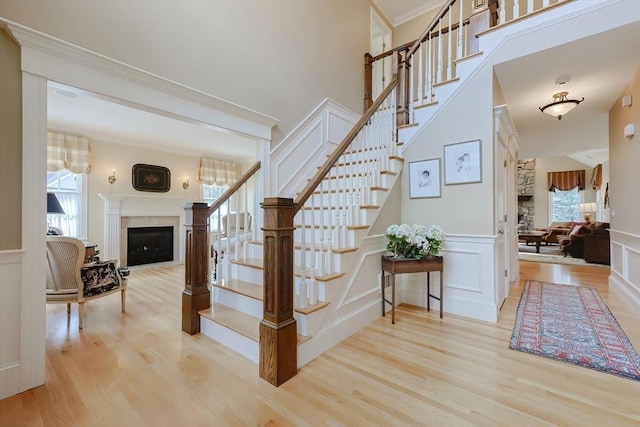 stairs with crown molding, a wainscoted wall, a decorative wall, a fireplace, and wood finished floors