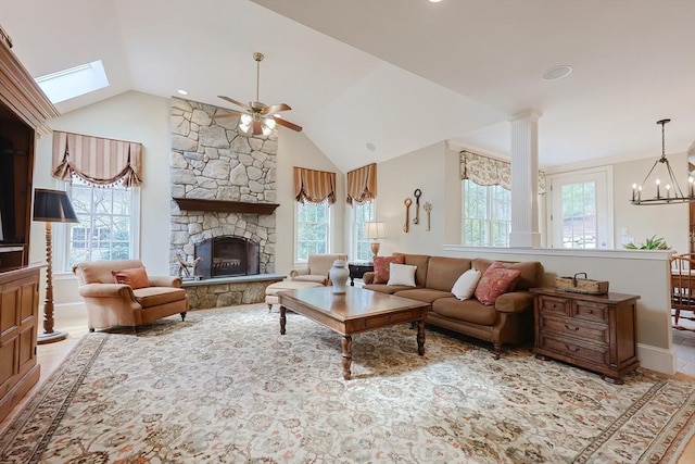 living room with lofted ceiling with skylight, a stone fireplace, and ceiling fan with notable chandelier