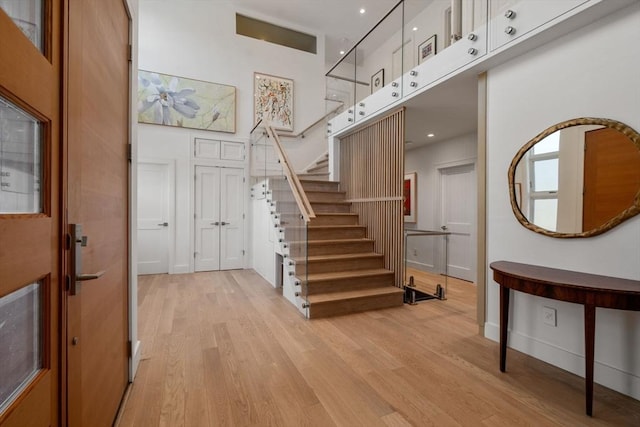 entrance foyer featuring stairway, light wood-type flooring, and a towering ceiling