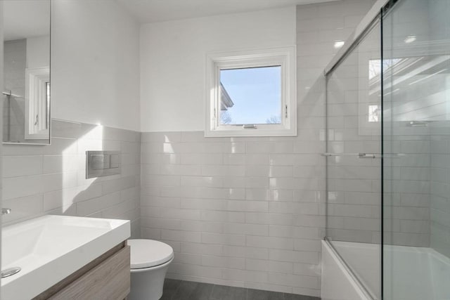 full bath featuring toilet, shower / bath combination with glass door, vanity, and tile walls