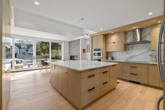 kitchen with tasteful backsplash, light brown cabinetry, light wood-style floors, modern cabinets, and wall chimney exhaust hood