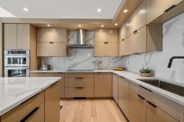 kitchen featuring black electric stovetop, stainless steel double oven, light brown cabinets, a sink, and wall chimney exhaust hood