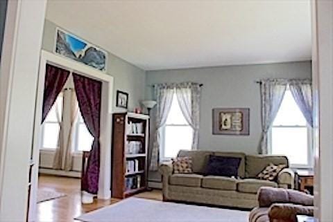374 Swains Pond Ave, Melrose, MA 02176 - living area with plenty of natural light, a baseboard radiator, and wood finished floors