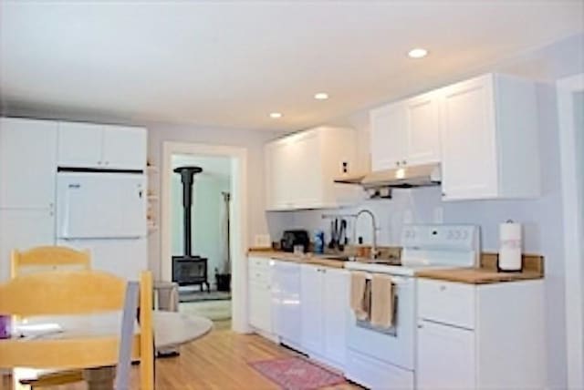 374 Swains Pond Ave, Melrose, MA 02176 - kitchen featuring white appliances, under cabinet range hood, a sink, a wood stove, and white cabinetry