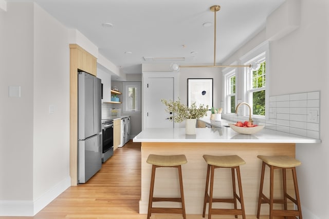 kitchen featuring kitchen peninsula, decorative backsplash, a breakfast bar area, appliances with stainless steel finishes, and light wood-type flooring