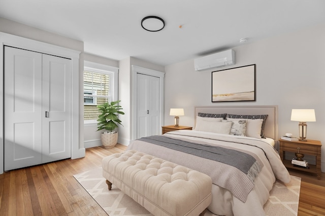 bedroom featuring light hardwood / wood-style floors, multiple closets, and a wall mounted AC