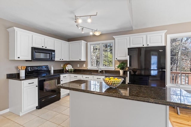 kitchen with light tile patterned floors, a sink, white cabinetry, dark stone counters, and black appliances