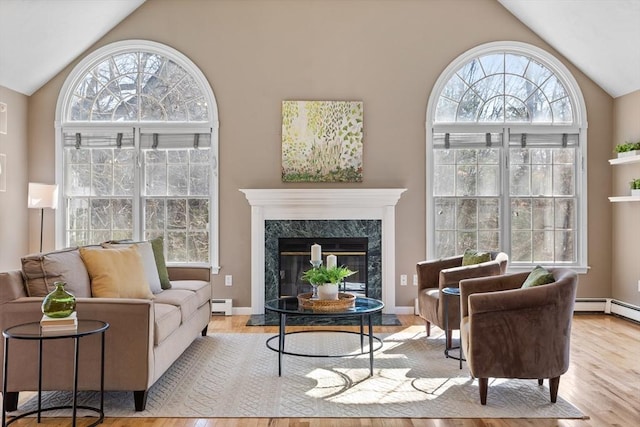 living area featuring a baseboard heating unit, vaulted ceiling, wood finished floors, and a high end fireplace