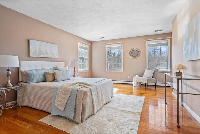 bedroom with baseboard heating, wood finished floors, visible vents, and baseboards